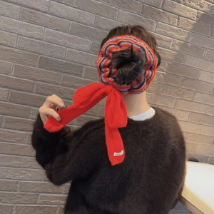 Close-up of a striped knitted scrunchie with a red ribbon bow and NICE label on hair