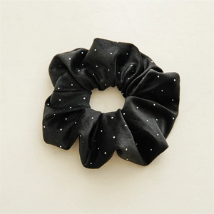 Détail du chouchou en velours noir à pois blancs et texture élastique sur fond beige