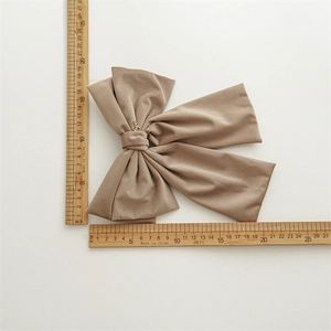 Detailed view of a large beige velvet bow hair clip with a gold charm and ruler for scale