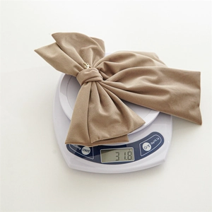 Detail showing high-quality velvet bow hair clip with gold logo metal charm on weighing scale