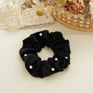 Detailed macro view of black velvet scrunchie with elegant white pearl bead embellishments