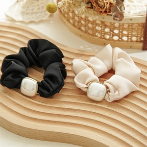 Detail of velvet scrunchies with square pearls on a wooden tray for elegant hair styling
