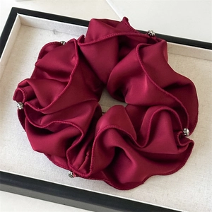 Macro shot of wine red satin scrunchie with rhinestones and elegant folded texture