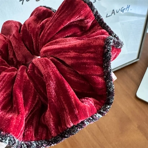 Gros plan d'un chouchou géant en velours rouge avec bordure en tweed sur surface en bois