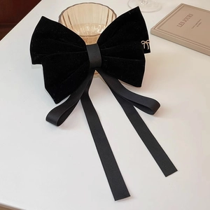 Detail of elegant black velvet bow hair clip with long ribbons and small gold charm