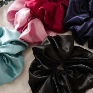 Gros plan de cinq grands chouchous en satin de couleurs bleu clair, rose, rouge, marine et noir