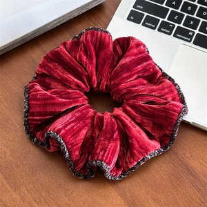 Détail d'un grand chouchou en velours rouge foncé avec une bordure à carreaux fins