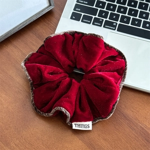 Détail d'un chouchou en velours rouge avec bords à volants et étiquette de marque