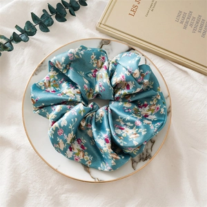 Chouchou en satin à fleurs bleu canard sur un plateau en marbre avec de l'eucalyptus
