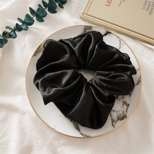 Détail d'un grand chouchou en satin noir brillant sur un plateau en marbre élégant