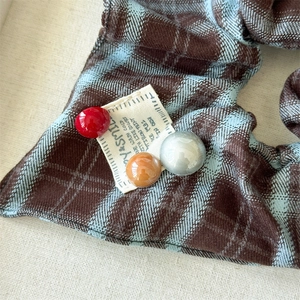 Close-up of red and blue plaid fabric scrunchie with colorful resin beads and woven label