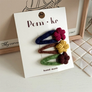 Three handmade felt floral hair clips for kids in navy, brown and green on a display card