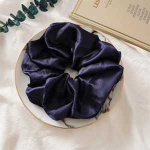 Détail d'un grand chouchou en satin foncé sur plateau en marbre au style élégant