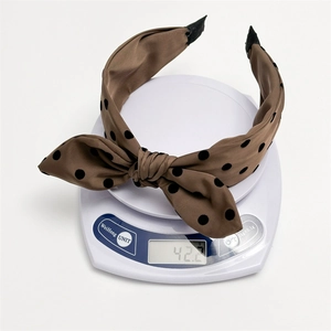 Polka dot bow headband in brown satin fabric weighing 42.2g on a scale for women