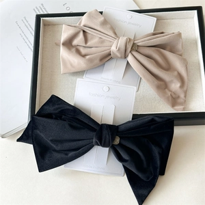 Detail showing two large velvet bow hair clips in black and beige with metal buckle accents