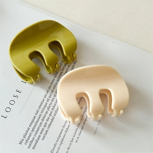 Close-up of M-shaped green and beige hair claws on a minimalist magazine layout