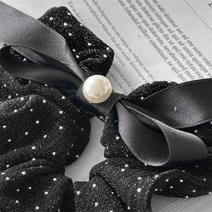 Macro shot of black sparkly fabric scrunchie with satin bow and pearl detail