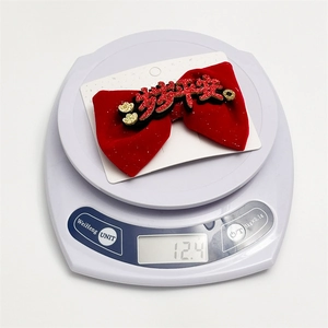 Detail of red velvet New Year bow clip weighing 12.4g on white digital scale