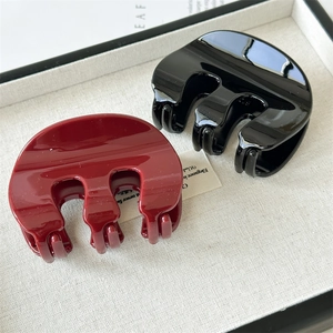 Detail view of large high-gloss black and deep red hair clips on a linen display tray