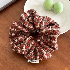 Détail du chouchou en tweed rouge avec fils dorés et étiquette tissée sur table bois