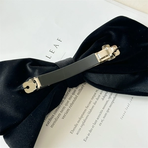 Elegant large black velvet bow hair clip with metal spring fastener on magazine background