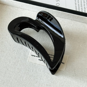 Detail of a gloss black heart-shaped hair claw clip on minimalist beige texture fabric