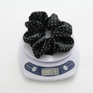 Close-up of a black polka dot scrunchie on a white scale showing 15.3g weight