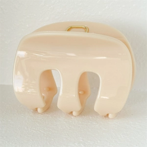 Macro shot of cream glossy hair claw clip with golden metal spring and smooth finish