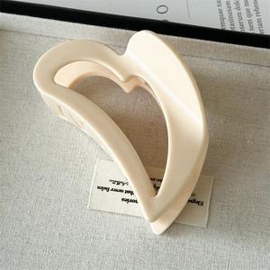Close-up of a matte cream hollow heart hair claw clip on a neutral linen surface