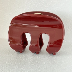 Detail of burgundy glossy hair claw clip featuring a metallic gold spring mechanism