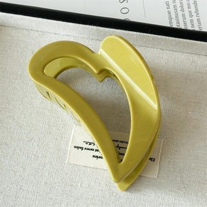 Detail of a glossy olive green heart-shaped hair claw clip on a decorative tray