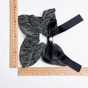 Detailed view of a black sparkling bow scrunchie with pearl measured on a scale
