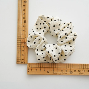 Detailed view of a white polka dot scrunchie with pleated fabric next to wooden rulers