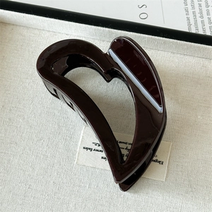 Detailed macro view of glossy burgundy heart hair claw clip on white textured tray