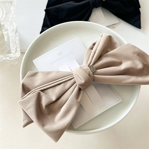 Detail of a large beige velvet bow hair clip with a gold metal centerpiece on a display card