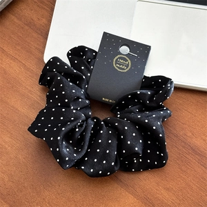 Close-up of elegant black polka dot satin scrunchie with handmade craft card on a wooden desk