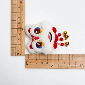 Détail d'une pince à cheveux lion en peluche avec perles rouges et cloches sur blanc