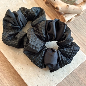 Detail of black satin hair scrunchies with quilted texture on minimalist stone background