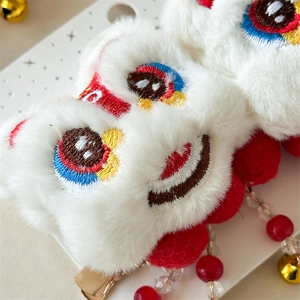 Détail de la barrette peluche lion avec pompons rouges et cloches dorées pour enfant