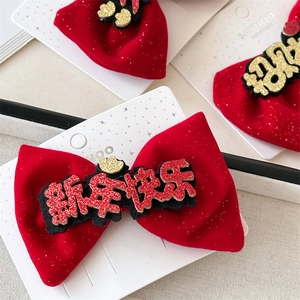 Detailed close-up of a red velvet bow hair clip with gold Happy New Year calligraphy