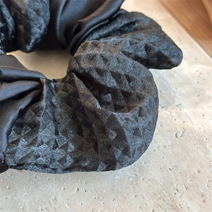 Macro view of black satin hair scrunchie with 3D diamond texture and fabric stitching