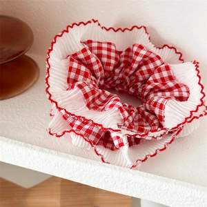 Red and white checkered scrunchie with lace edges on a white stone background