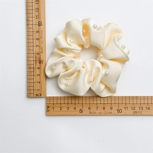 Détail d'un chouchou en satin crème de 11cm avec perles blanches présenté sur une règle