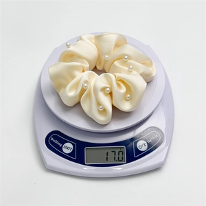 Détail d'un chouchou en satin crème avec perles pesant 17g sur une balance numérique