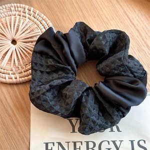 Detailed view of large black scrunchie combining shiny satin and diamond quilted fabric