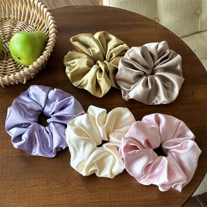 Dettaglio di cinque scrunchies in raso colorato esposti su un tavolo di legno