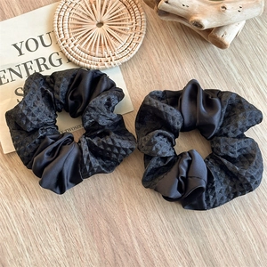 Close-up of dual-texture black scrunchies with embossed fabric and satin on wooden surface