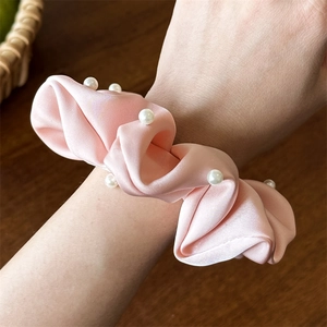 Détail d'un chouchou en satin rose orné de perles blanches porté au poignet