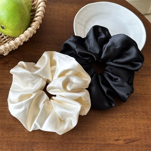 Set di elastici per capelli in raso nero e bianco crema su un tavolo in legno rustico