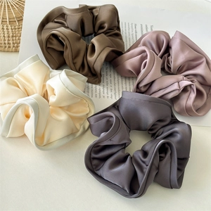 Detailed view of satin scrunchies in coffee, pink, white, and grey with silk texture